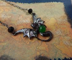 a close up of a necklace with a dragon on it's back and green beads