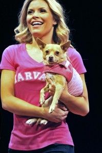 a woman holding a small dog in her arms and smiling at the camera while standing on stage