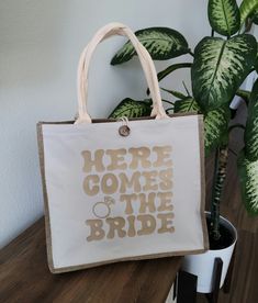 a white bag with the words here comes the bride printed on it next to a potted plant