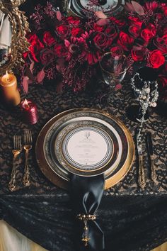 the table is set with black and gold plates, silverware, and red roses