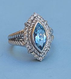 Judith Ripka Blue Topaz and CZ Sterling Silver Ring - Size 11 Marquise cut blue topaz bezel set with a twisted rope border, with 20 round CZs surrounding the blue topaz. Thick double cable band which tapers to a solid band in the back. The underside has Judith Ripka's signature fleur-de-lis cut-out. In great vintage condition. Fit: Sits on the ring mandrel at exactly size 11, and fits as a size 11. 11.58 grams Marked: Judith Ripka, 925, Thailand, CZ  Photos taken outside in natural light. Kindly disregard any weird reflections on the silver, (such as green tinting from the trees).  In very good vintage condition, but might have wear consistent with a well-loved piece. ba5634 Blue Aquamarine Diamond Ring, Luxury Blue Marquise Cut Jewelry, Blue Diamond Marquise Jewelry, Sapphire Rings With Diamond Accents And Blue Topaz, Sapphire Colored Blue Topaz Rings With Diamond Accents, Blue Marquise Diamond Jewelry, Blue Cubic Zirconia Rings With Diamond Accents, Blue Marquise Diamond Ring With Center Stone, Blue Marquise Cut Ring With Center Stone