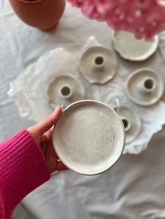 a person holding a cup in front of some cups and saucers on a table