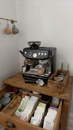 an espresso machine sitting on top of a wooden drawer filled with cups and saucers