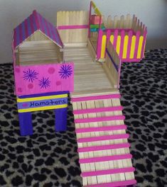 a pink and purple wooden toy house on top of a leopard print floor with stairs leading up to it