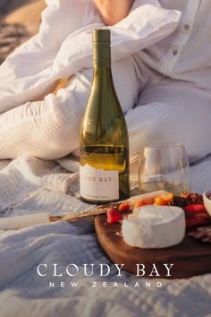 a bottle of wine sitting on top of a bed next to a plate of food