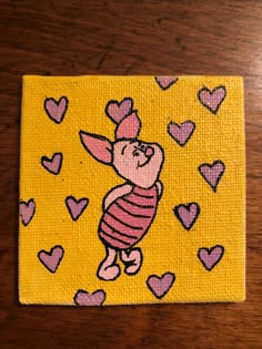 a painting of a winnie the pooh character with hearts on yellow fabric, sitting on a wooden surface