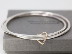 "Welcome to Silver Cave Designs. The listing is for a simple yet beautiful handmade sterling silver twin set of round bangles, and with a SOLID 9ct yellow gold heart charm attached on it. This sterling silver and gold heart bangle is available in 58mm, 63mm and 68mm. Hand-made and tumbled for 24 hours, the sterling silver twin set of bangles is sturdy and comfortable to wear. The gold heart charm adds a hue of bright colour and a special message to this bangle. It certainly makes a great jewelle Silver Jewlery, Handmade Silver Jewellery, Antique Silver Jewelry, Silver Jewelry Design, Twin Set, Silver Jewelry Handmade, Silver Bangle Bracelets, Sterling Silver Bangles, Silver Bangle