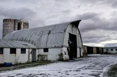 an old barn with snow on the ground and two silos in front of it