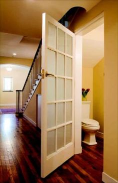 an open door leading to a bathroom and toilet in a house with hardwood floors, walls and stairs