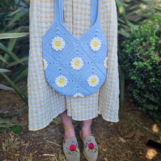 a woman is wearing a blue crocheted bag with daisies on the front