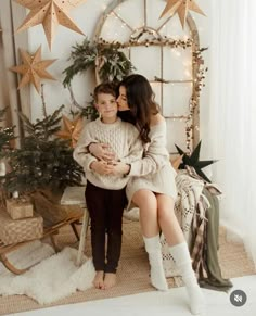 a mother and son sitting on a chair in front of a christmas tree