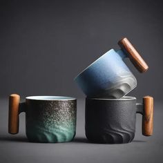 two mugs with wooden handles are stacked on top of each other in different colors