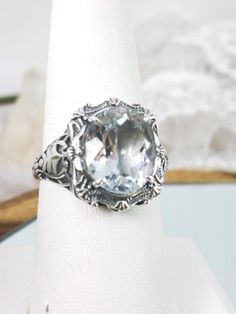 Oval Gem Sterling Silver Filigree RingBeauty Design#D229 Introducing the magnificent D229 Beauty Ring, a brand-new Vintage reproduction sterling silver filigree ring. The perfect oval-cut natural gemstone is a jaw-dropping sight. The gemstone is 12mm by 10mm (just shy of 3/8" inch) in size, while the ring itself is 5/8th of an inch (16.5mm) in length and sits 7mm off the finger. This exquisite rendition of a vintage design filigree ring is one of a kind and is sure to make heads turn when you wa Oval Large Stone Moonstone Wedding Ring, White Oval Topaz Ring For Gift, White Oval Topaz Ring Gift, Classic Silver Topaz Ring With Gemstone Accents, Oval Blue Topaz White Ring, White Oval Blue Topaz Ring, Silver Oval Topaz Ring, Oval Large Stone Topaz Ring For Anniversary, Oval Topaz Ring With Large Stone For Anniversary