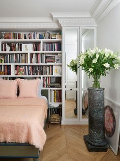 a bedroom with a bed, bookshelf and flowers in vases on the floor