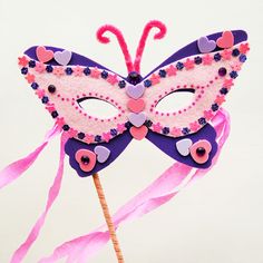 a pink and purple mask with hearts on it sitting on top of a wooden stick