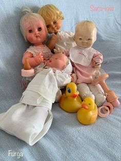 a group of dolls sitting on top of a bed next to rubber ducky toys