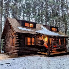 a log cabin in the woods with snow on the ground and lights shining from windows