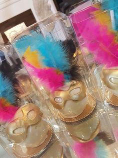 there are some colorful feathers on top of masks in plastic containers with gold trimmings