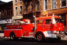 an old red fire truck parked on the side of the road in front of buildings