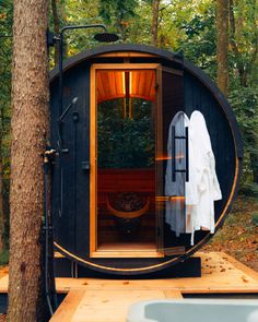 an outdoor sauna in the woods with towels hanging on it's side and trees around