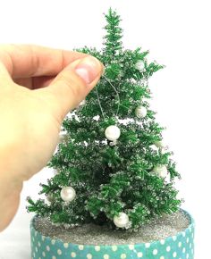 a small green christmas tree sitting on top of a blue and white polka dot ribbon