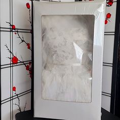 a white frame sitting on top of a table next to a vase with red flowers