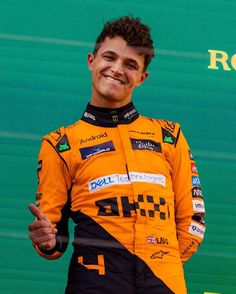 a man in an orange and black racing suit giving the peace sign with his hand