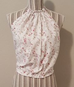 "I made this gorgeous bohemian style halter top repurposing linens, by pulling the neck and waist strings to tie where needed, this garment will fit from an x-small to a medium. The crocheted flower is also a pin to remove or place where desired. For a better visual, the mannequin's measurements are bust 34\"." Affordable Multicolor Bohemian Halter Top, Hippie Sleeveless Halter Top For Spring, Bohemian Sleeveless Crop Top For Spring, Bohemian Floral Print Halter Top For Beach, Bohemian Sleeveless Halter Top For Spring, Bohemian Flowy Crop Top For Spring, Flowy Bohemian Crop Top For Spring, Bohemian Halter Top For Spring Festival, Bohemian Halter Top For Spring