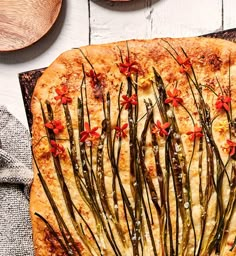 a pizza with red flowers on it sitting next to some wooden spoons and plates