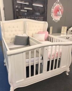 a white crib with pink and gray pillows on it's sides in a store