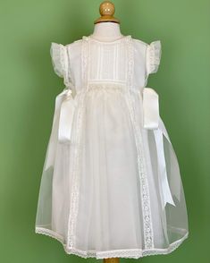 An elegant off-white dress that has a gorgeous detail in smock on the front with delicate laces. The dress has two satin ribbons on the side, and has buttons on the back for closure. Made in Spain Dry Clean Final sale, no exchanges nor returns are accepted Elegant White Dress For Confirmation, Elegant Dress With Lace Sleeves For Confirmation, Elegant Confirmation Dress With Lace Sleeves, Elegant Summer Lace Dress For First Communion, White Spring Dresses With Ribbon Detail, White Spring Dress With Ribbon Detail, White Dress With Ribbon Detail For Spring, Elegant Lace Dress For First Communion, Elegant Lace Dress With Lace Bodice For Confirmation