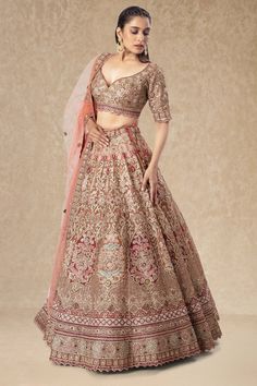 a woman in a brown and pink lehenga is standing with her hands on her hips