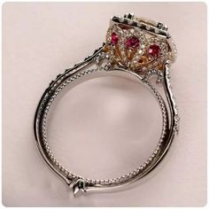 a fancy ring with red and yellow stones on it's sides, sitting on a white surface