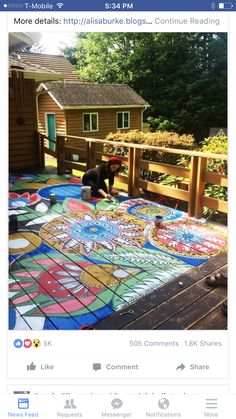 a person painting on the ground in front of a wooden fence with flowers and plants