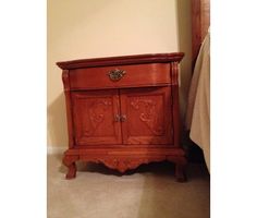 a small wooden cabinet sitting in the corner of a room next to a bed and nightstand