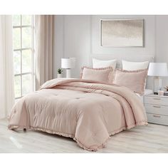 a bed with pink comforter and pillows in a room next to a white dresser