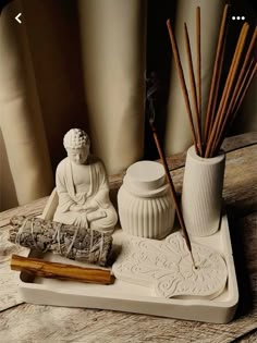 a white statue sitting on top of a wooden table next to a vase and incense sticks