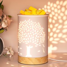 a white and gold lamp with a tree on it next to a vase filled with flowers