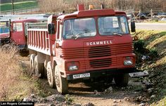 an old red truck parked on the side of a dirt road