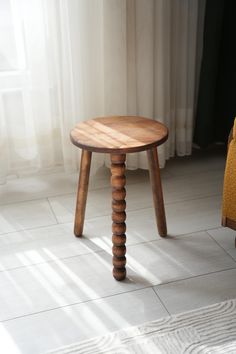 a small wooden stool sitting on top of a white tile floor next to a window