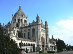 a large white building with many windows and spires on it's side, surrounded by trees