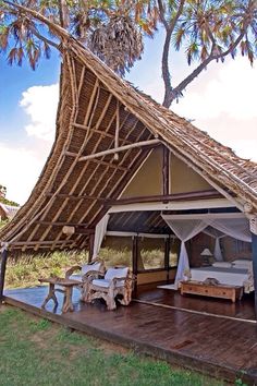 an outdoor bedroom with a thatched roof and wooden flooring, surrounded by palm trees