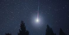 a bright light shines in the night sky above some trees and snow covered ground