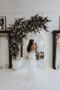 a woman standing in front of a mirror wearing a wedding dress with flowers on it