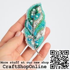 a hand holding a beaded brooch with a feather on it's side