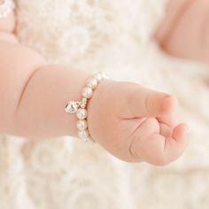 Baby girl wearing the white luster pearl bracelet around her wrist, part of our baby jewelry collection. Elegant Hypoallergenic Heart-shaped Charm Bracelet, Elegant Hypoallergenic Heart Charm Bracelet, Heart-shaped Pearl Bracelet For Wedding, Elegant White Pearl Bracelet With Heart Charm, Elegant White Heart Bracelet For Wedding, Classic White Jewelry With Heart Charm, Classic Personalized White Pearl Bracelet, Elegant Pearl Bracelet With Heart Beads For Mother's Day, Pearl Heart Bracelet For Wedding