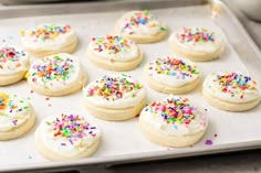 there are many cookies with white frosting and sprinkles on the pan