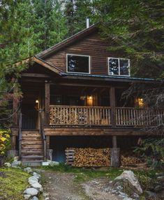 a cabin in the woods with lots of wood stacked on the porch and stairs leading up to it