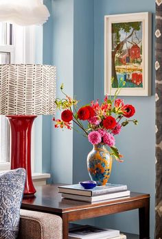 a vase filled with red and pink flowers on top of a table next to a lamp