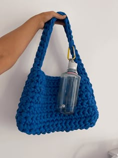 a hand holding a blue crocheted purse with a water bottle in the bottom